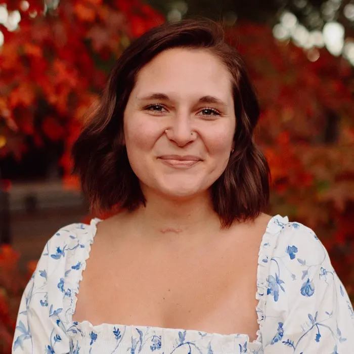MacKenzie Korsi Thomas smiling in front of autumn trees