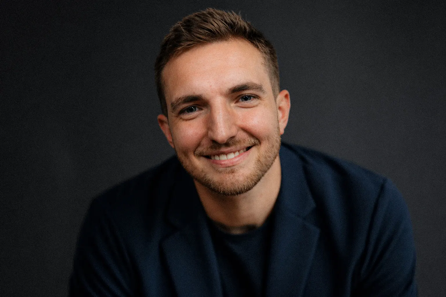 Riley Simpson smiling in a dark studio portrait